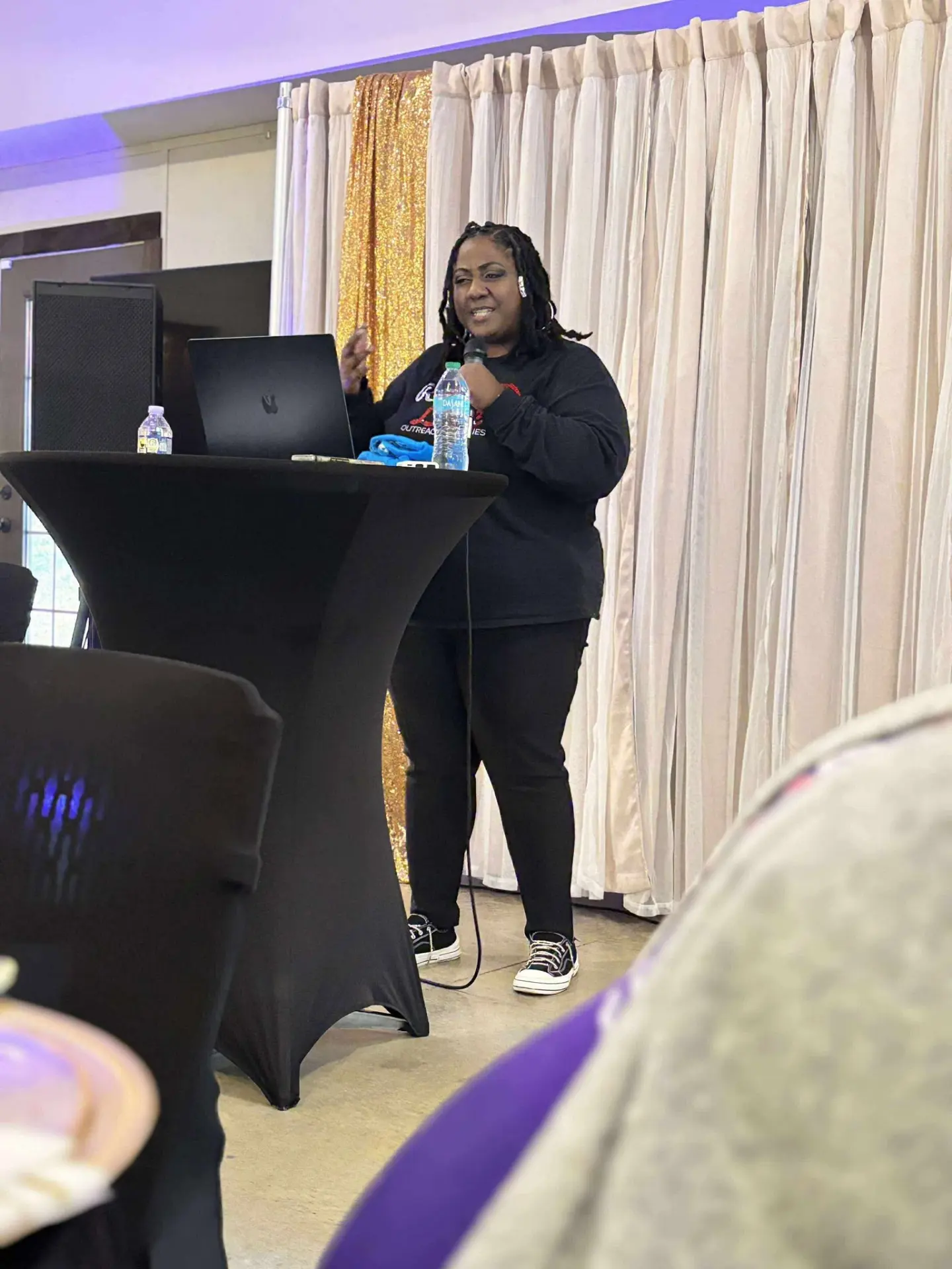 Rose Sherrod teaching from a standing table with a microphone during a women's session.