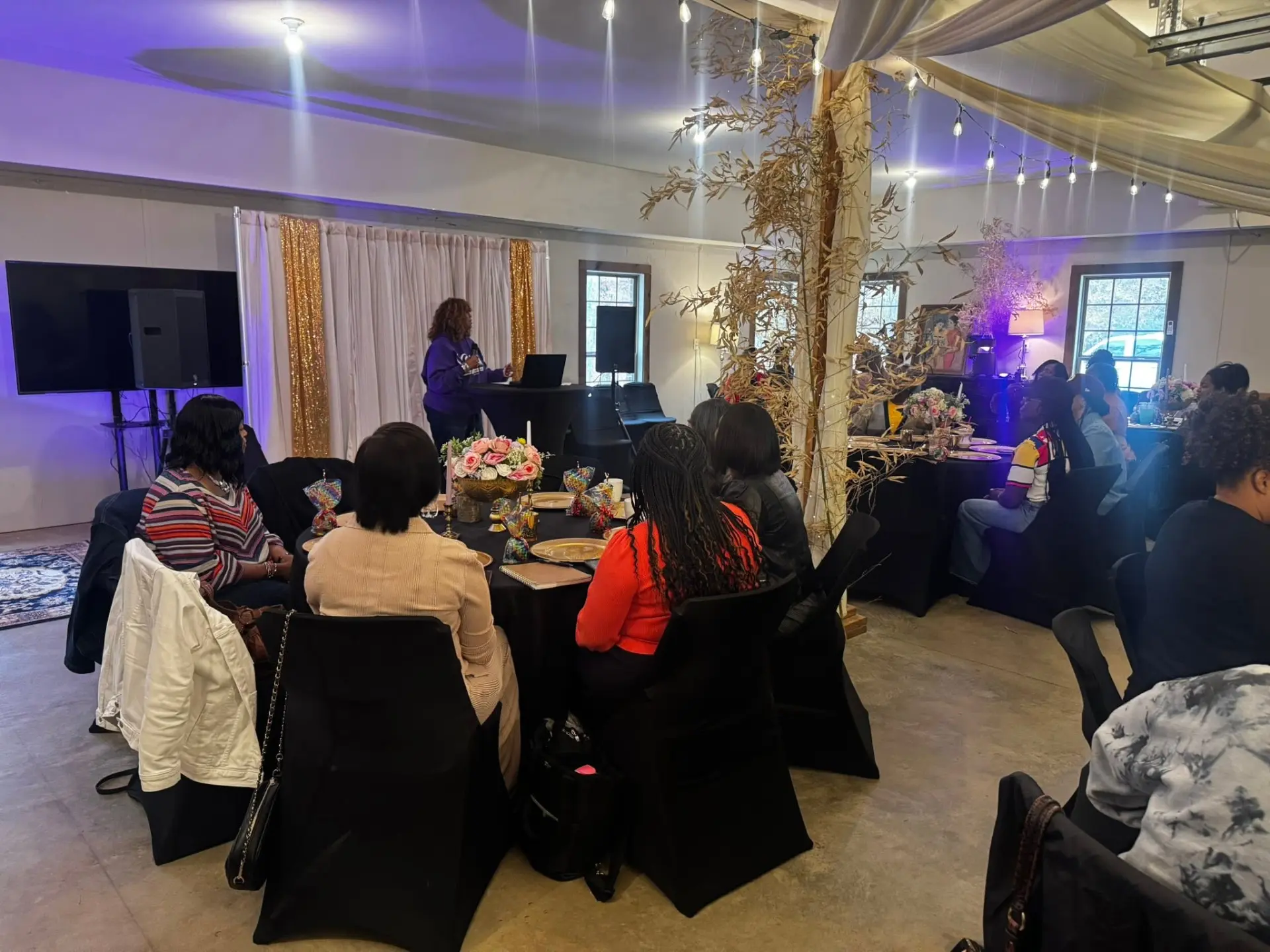 Women seated at candlelit tables listening to Pastor Emma White teach at a Daughters of Promise gathering.