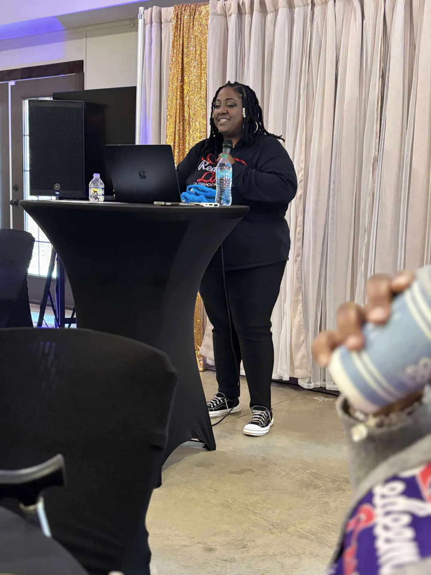 Rose Sherrod speaking with a microphone beside a laptop at a ministry event.