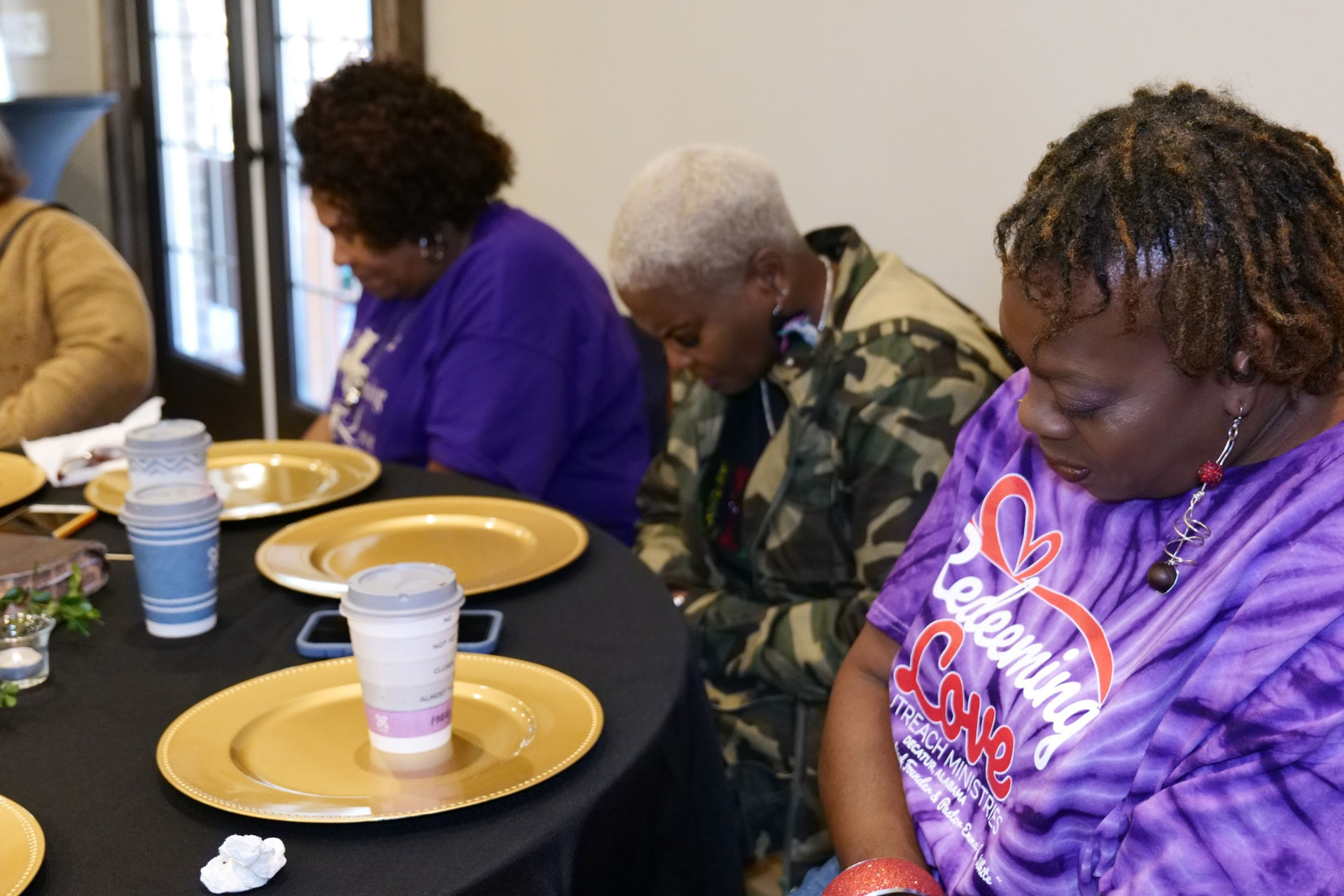 Women in Redeeming Love Outreach Ministries shirts seated together in a moment of prayer and reflection.